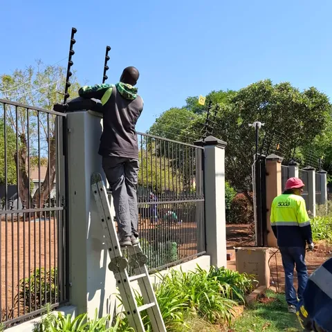 A man on a ladder fitting electric fence brackets to the top of a wall