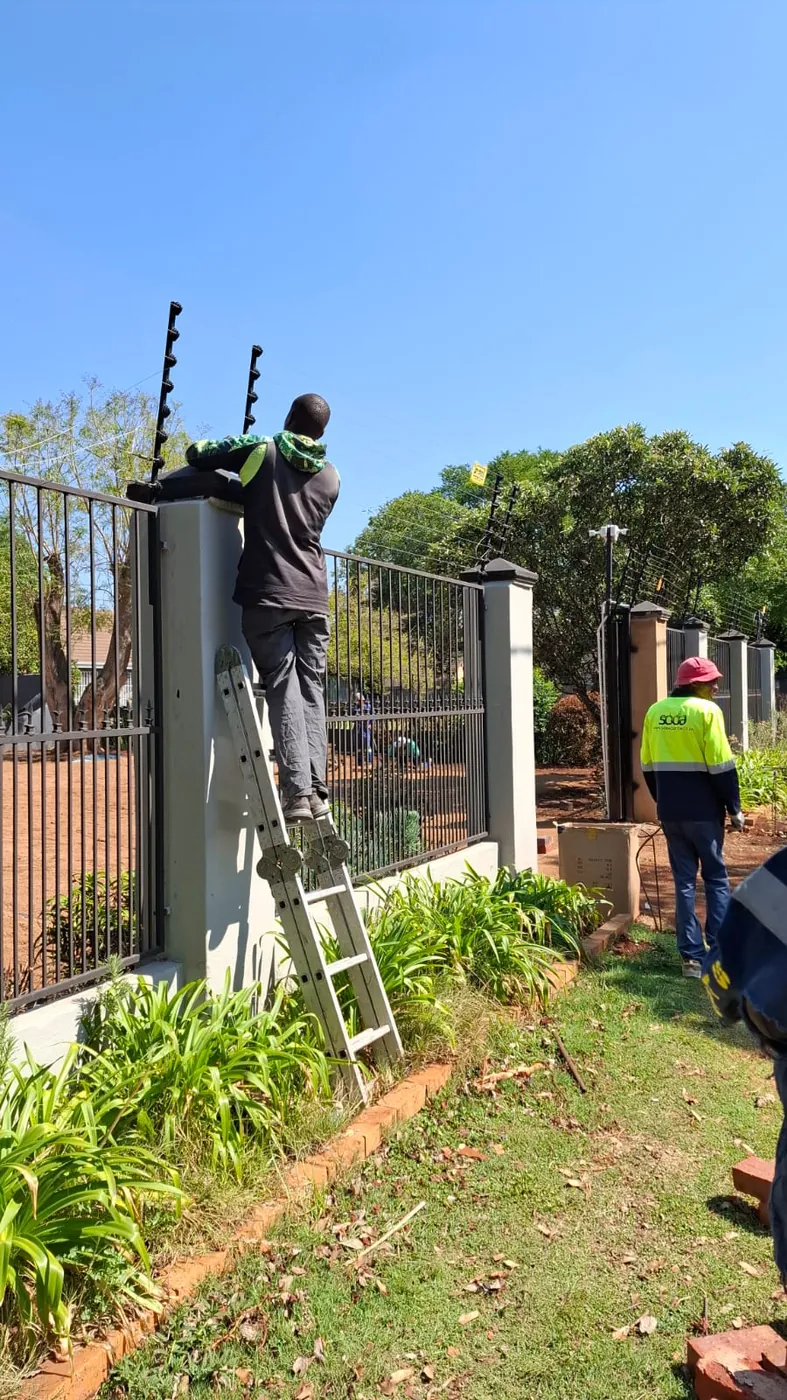 A man on a ladder fitting electric fence brackets to the top of a wall